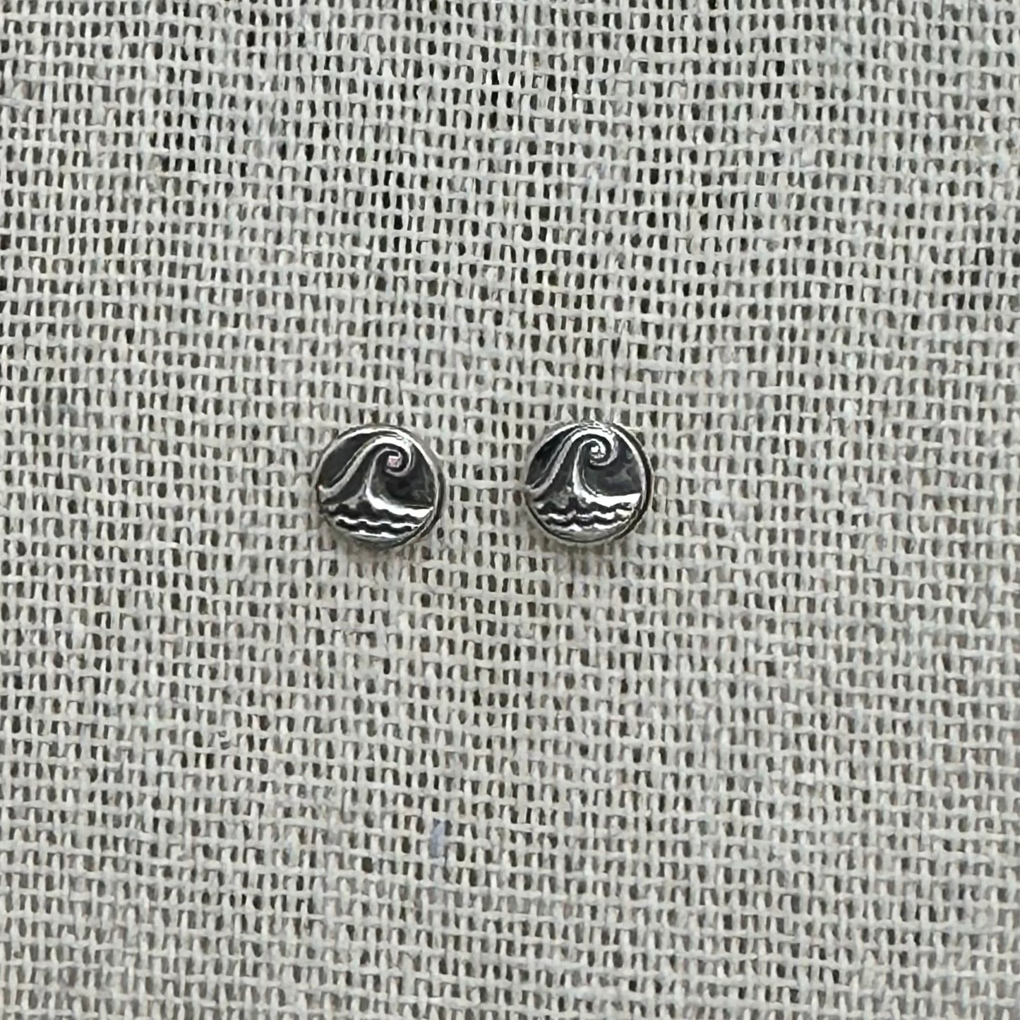 Close-up of the silver wave pebble earrings, highlighting the embossed details and patinated finish.