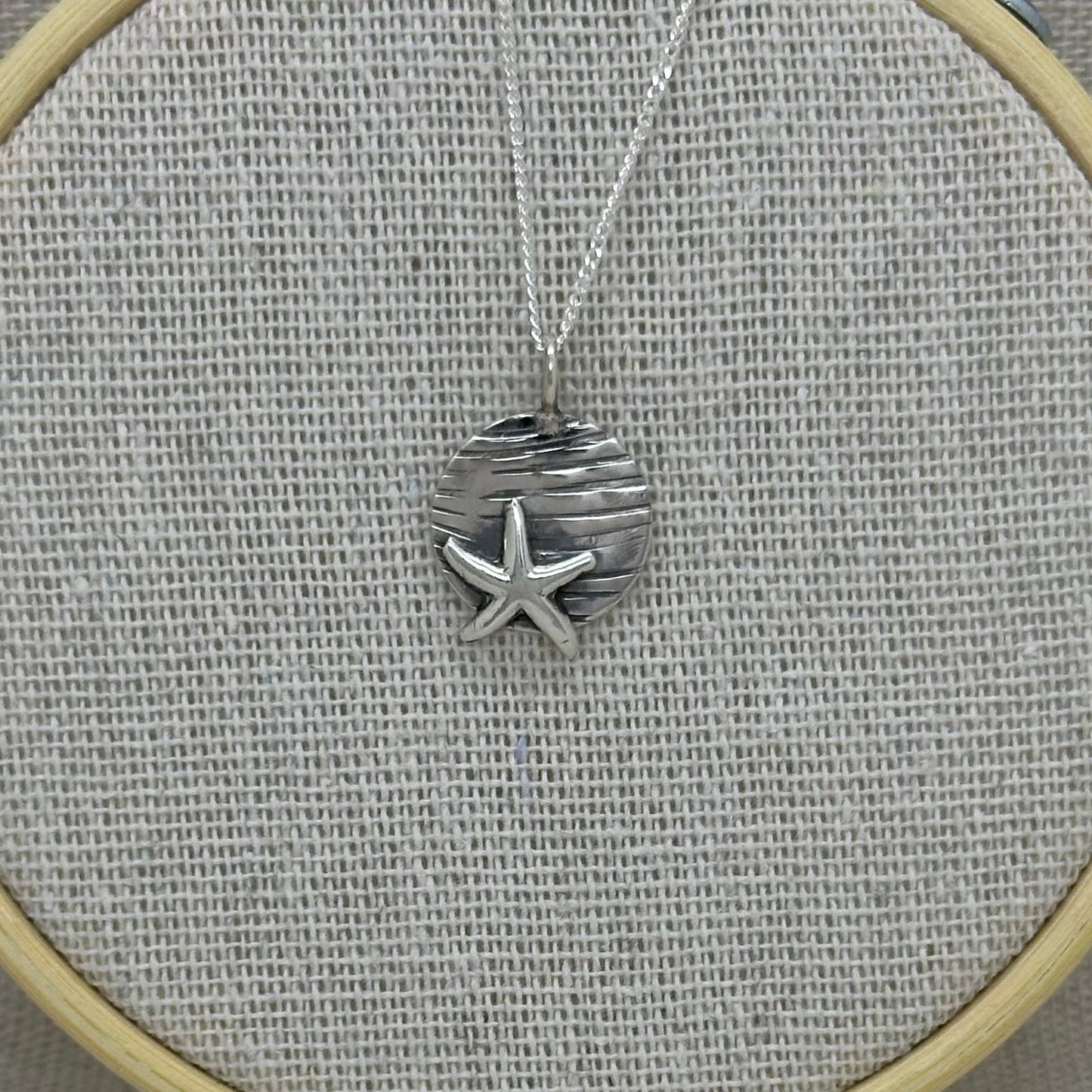Handmade sterling silver starfish pendant with a textured coin background, displayed on an 18-inch silver curb chain