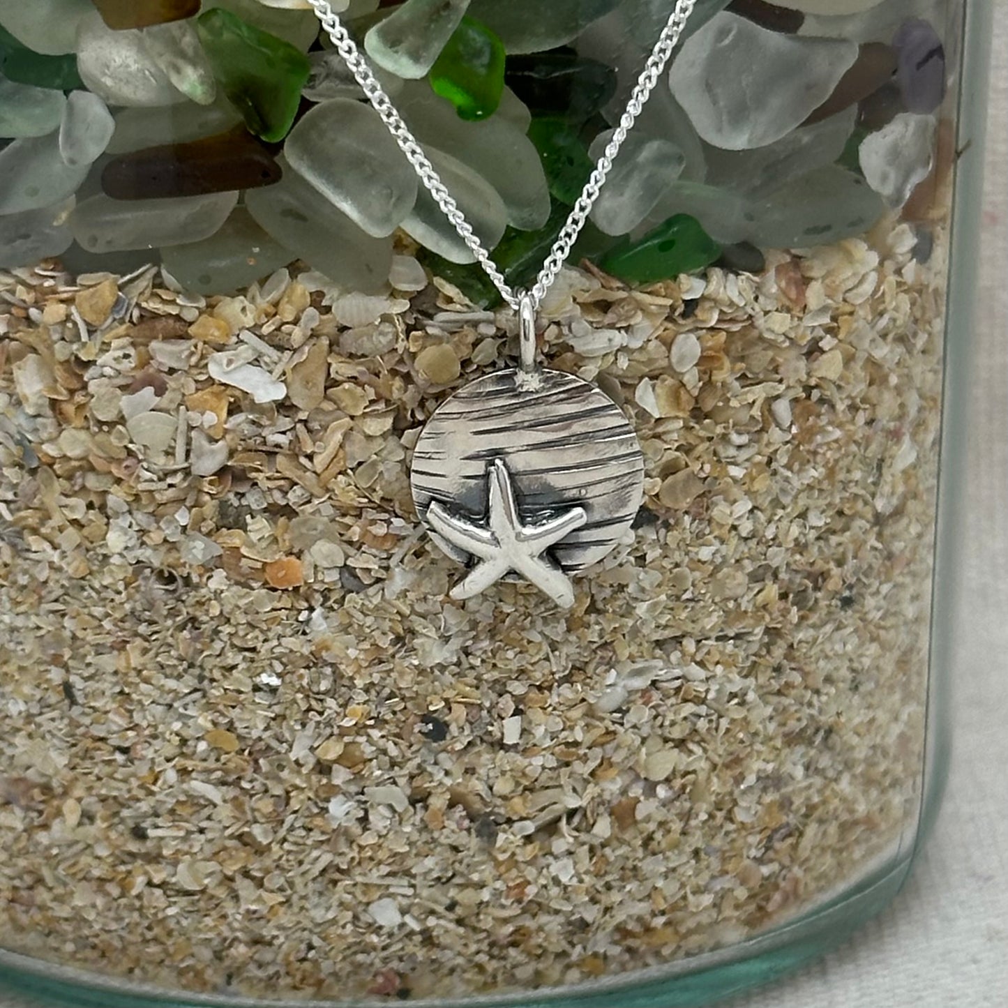 Close-up of the silver coin pendant, highlighting the contrast between the smooth starfish motif and the textured surface.