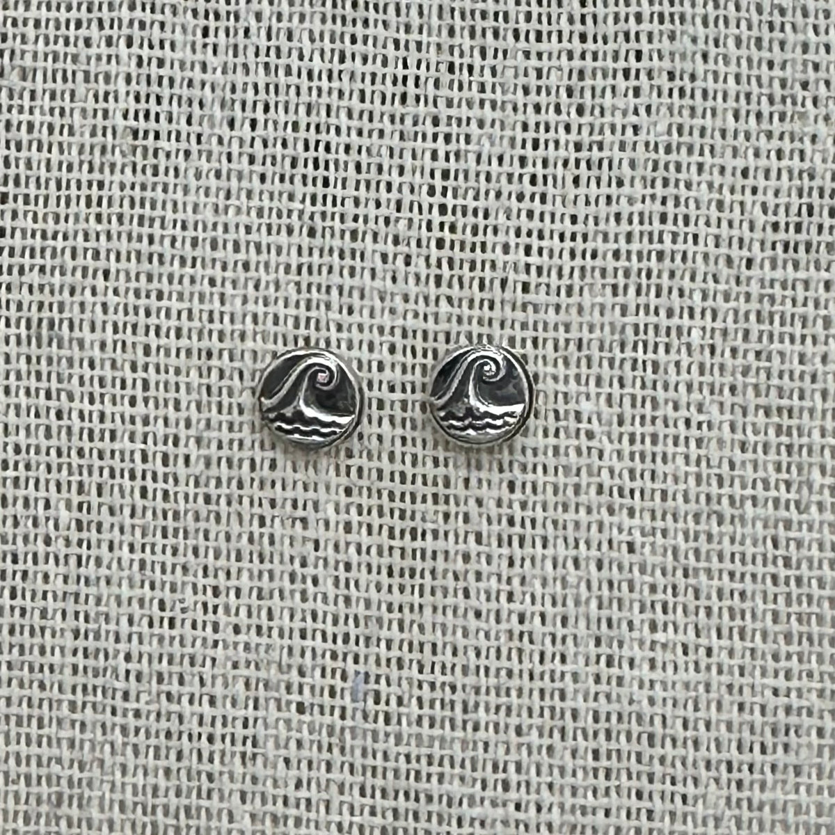 Close-up of the silver wave pebble earrings, highlighting the embossed details and patinated finish.