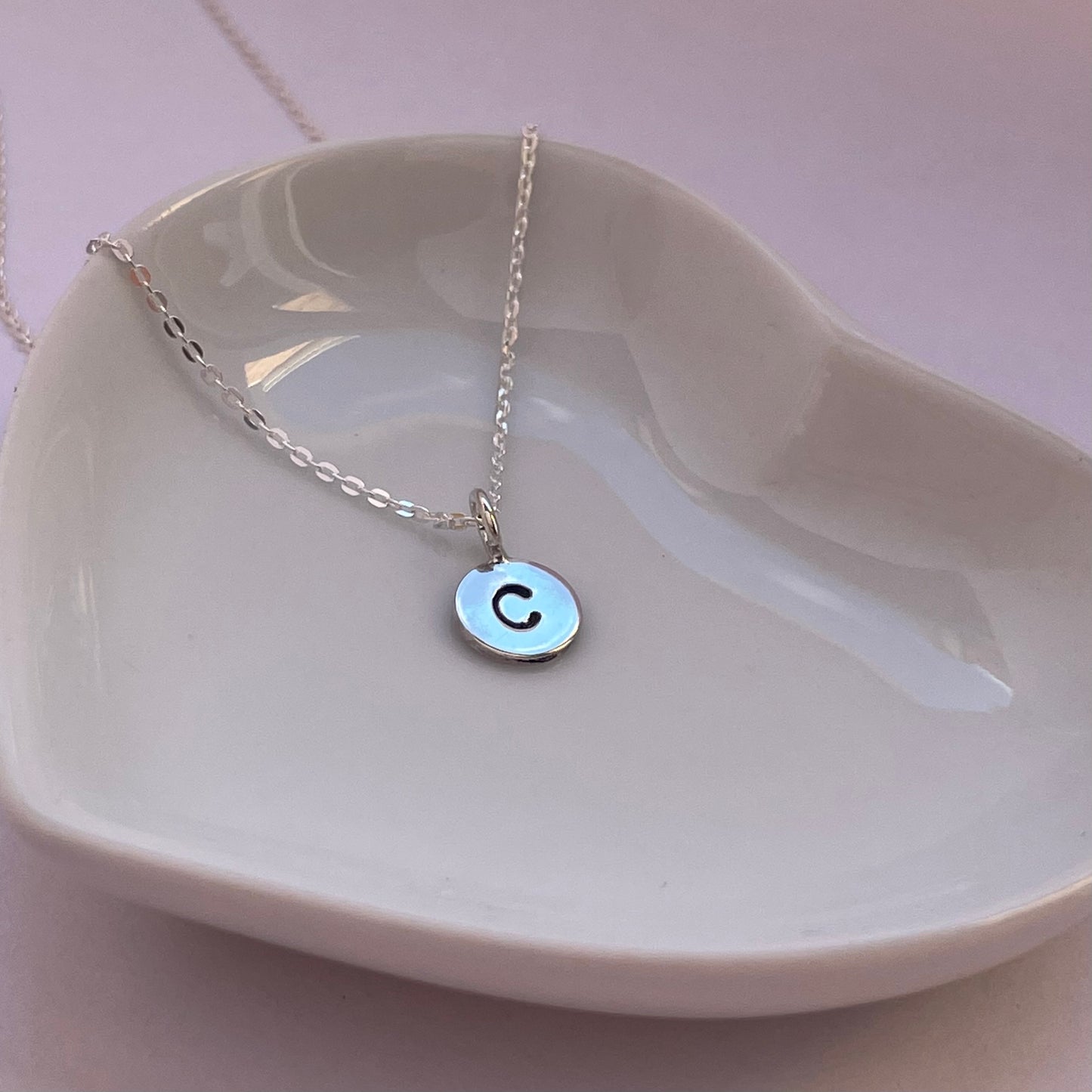 Close-up of the silver initial pendant, showcasing the hand-stamped custom letter and polished finish