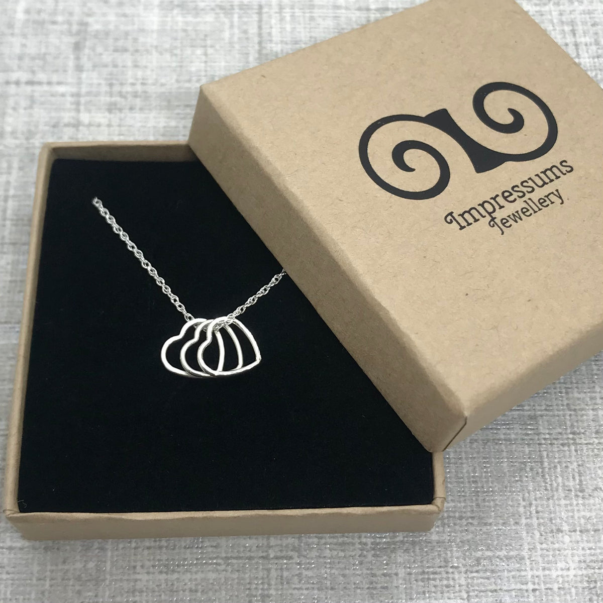 A sterling silver heart charm necklace in an Impressums Jewellery branded gift box, ready for gifting.