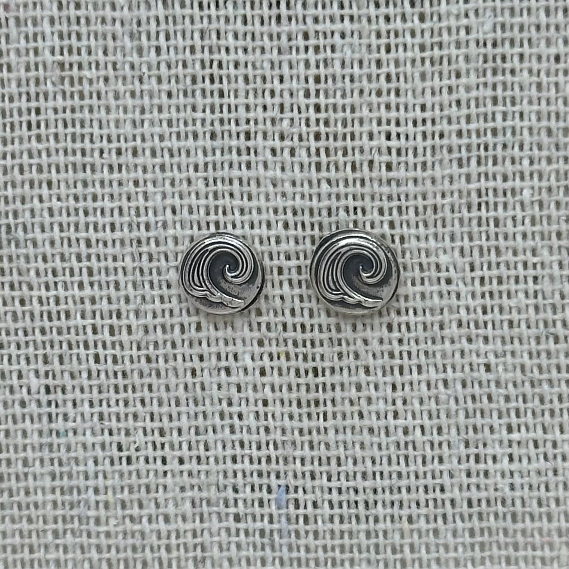 Close-up of the silver wave pebble earrings, highlighting the embossed details and patinated finish.