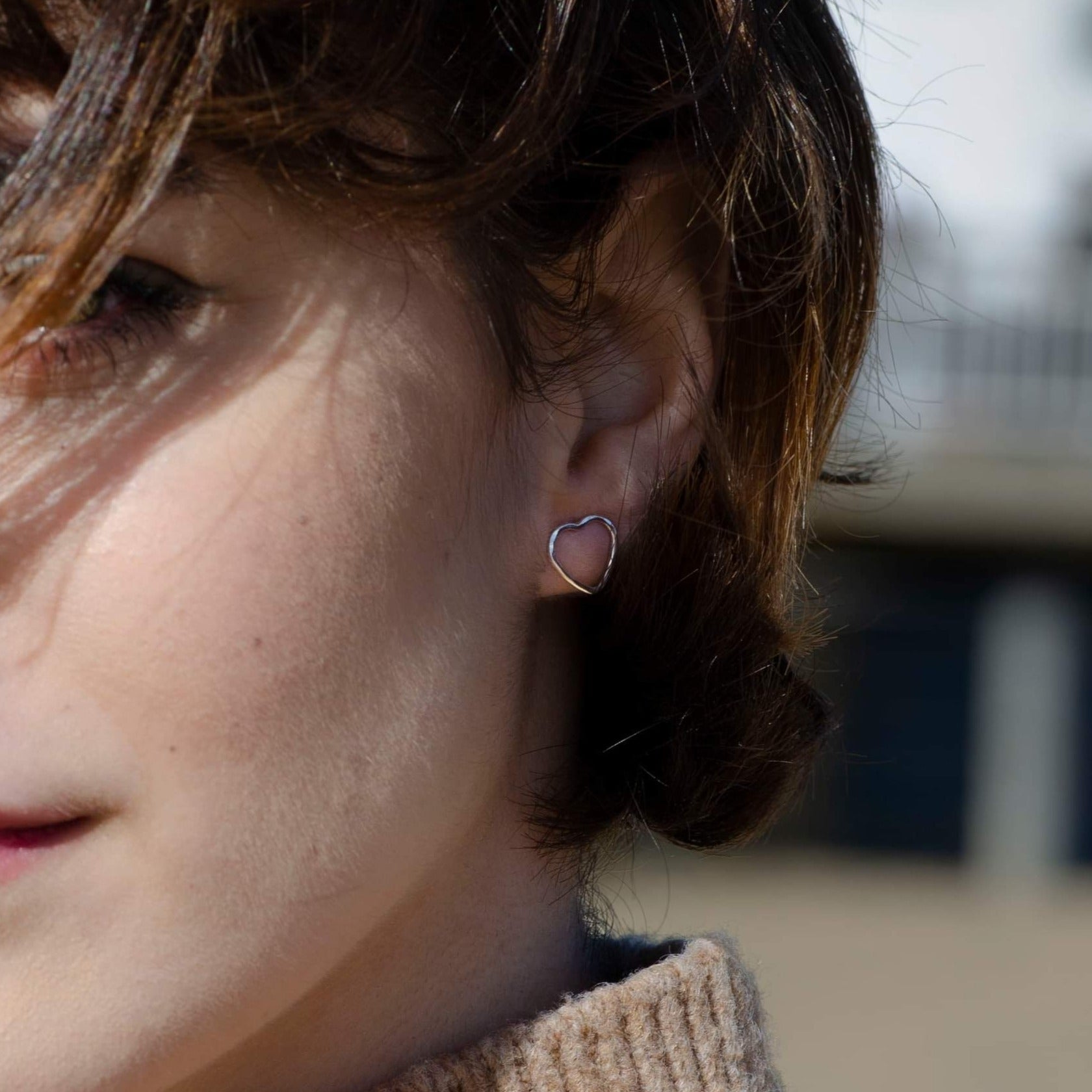 Minimalist hammered silver heart earrings being worn, showcasing their delicate and lightweight design.