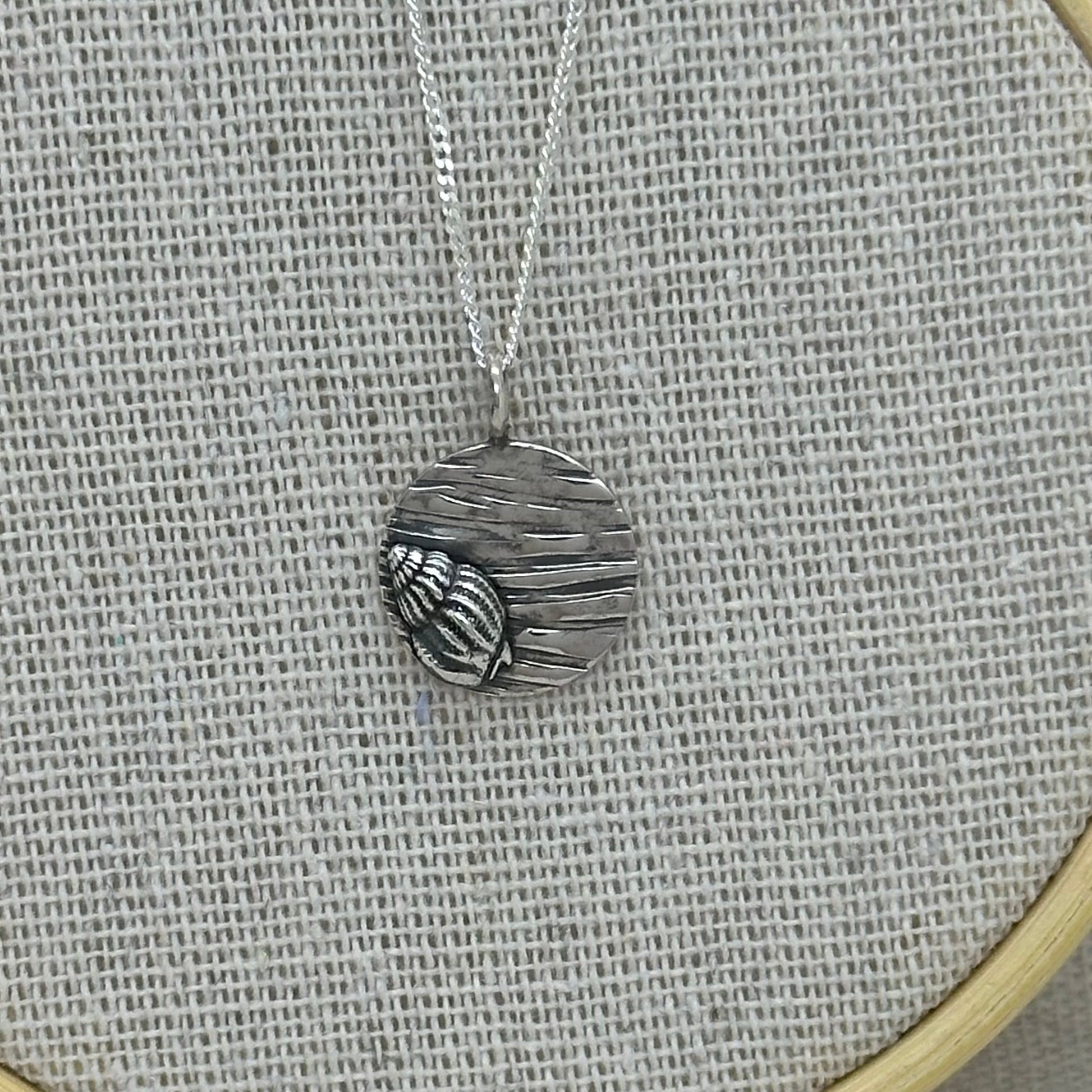 Close-up of the silver coin pendant, highlighting the contrast between the smooth spiral shell motif and the textured surface