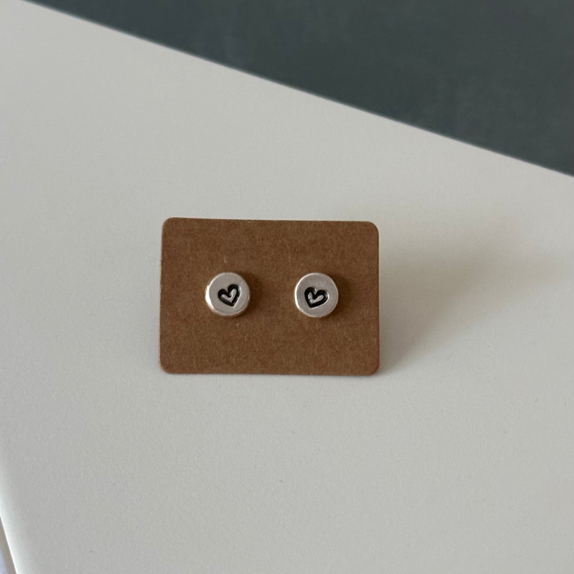 Close-up of handcrafted recycled sterling silver sweetheart studs with a delicate heart stamp on each flattened pebble earring