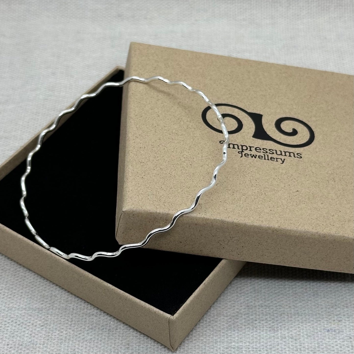 A sterling silver wavy bangle in an Impressums Jewellery branded gift box, ready for gifting.