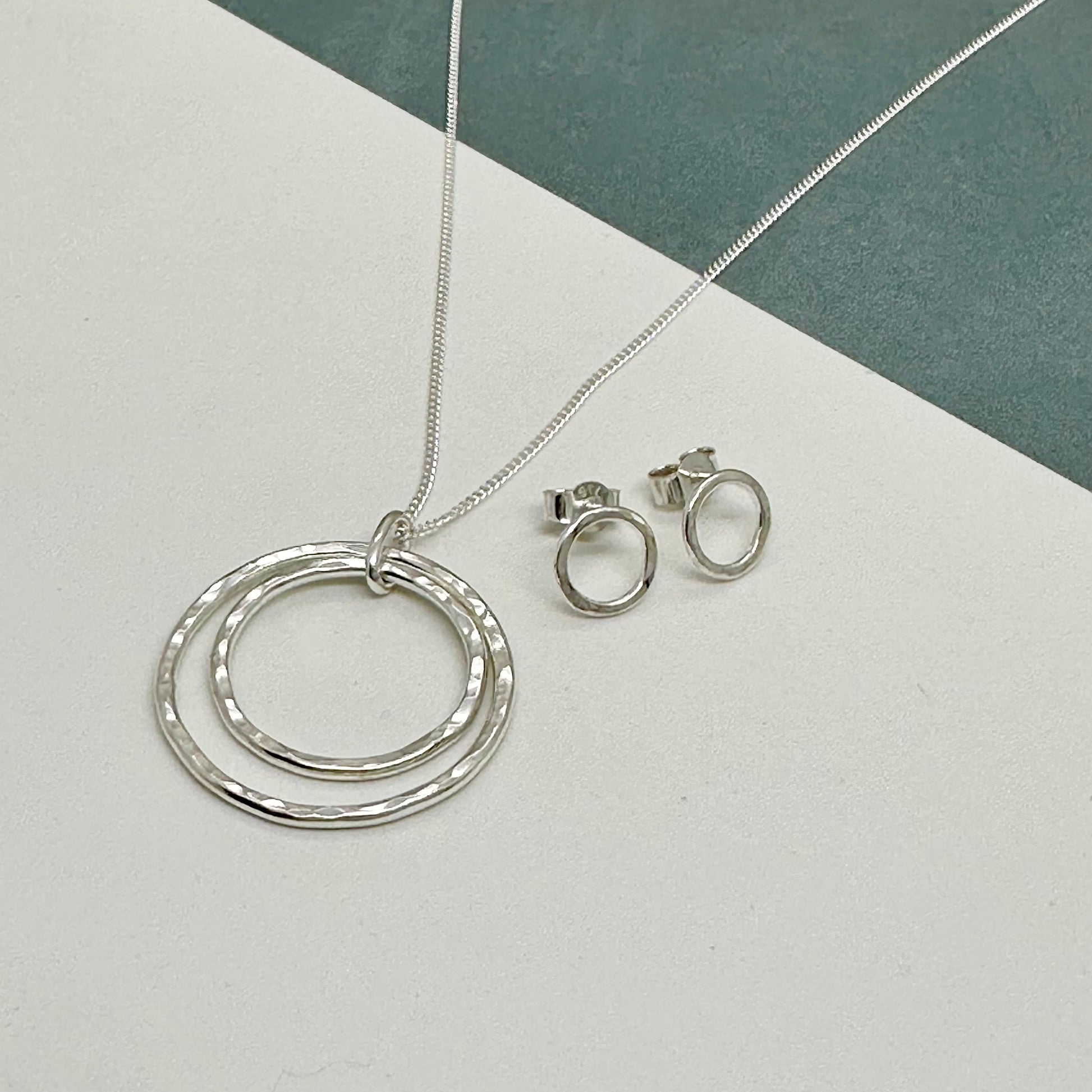 Close-up of interlocking hammered silver circles on a delicate sterling silver chain with matching 8mm sterling silver hammered stud earrings with a textured finish, designed to complement the pendant