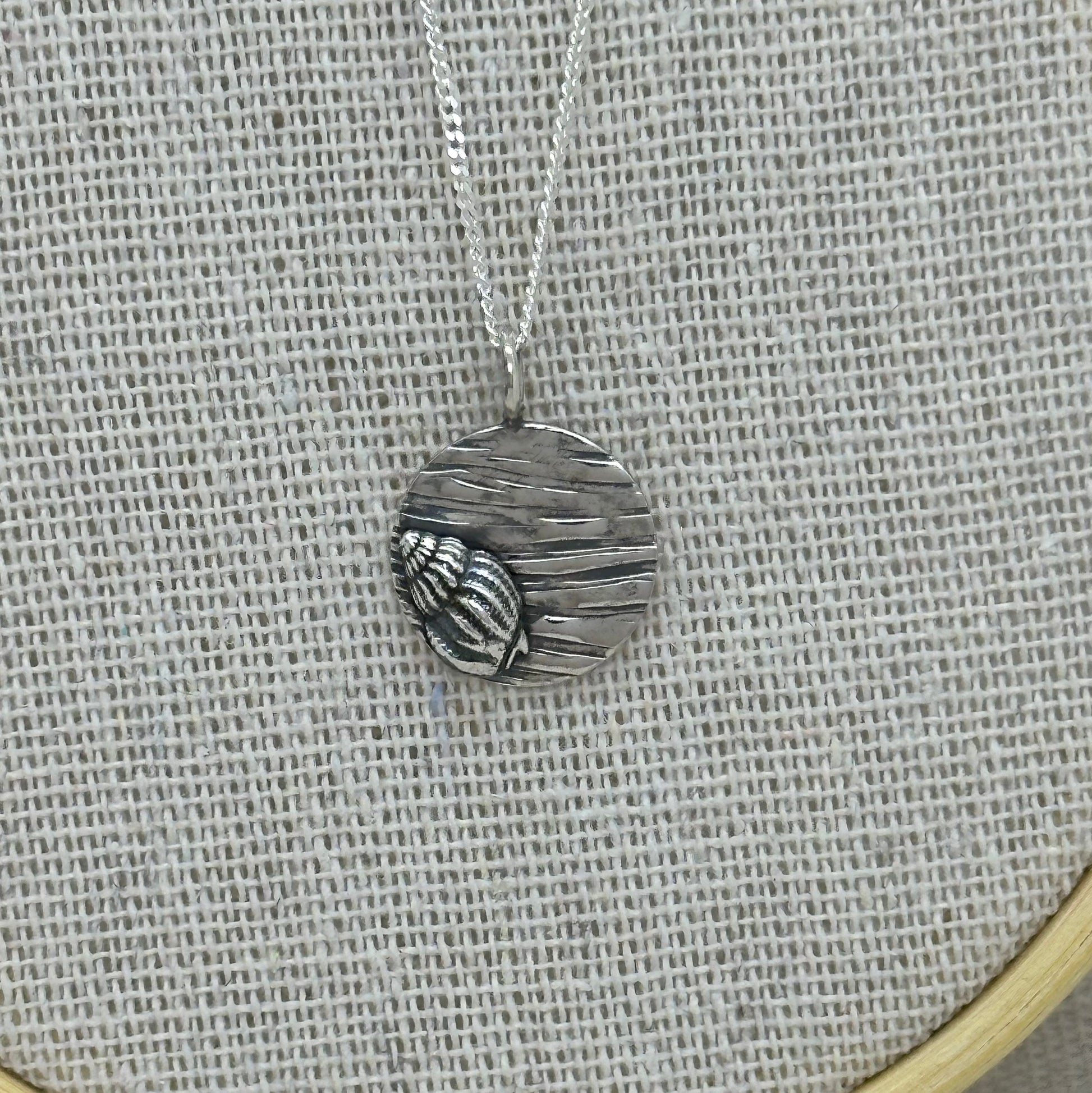 Handmade sterling silver shell pendant with a textured coin background, displayed on an 18-inch silver curb chain.