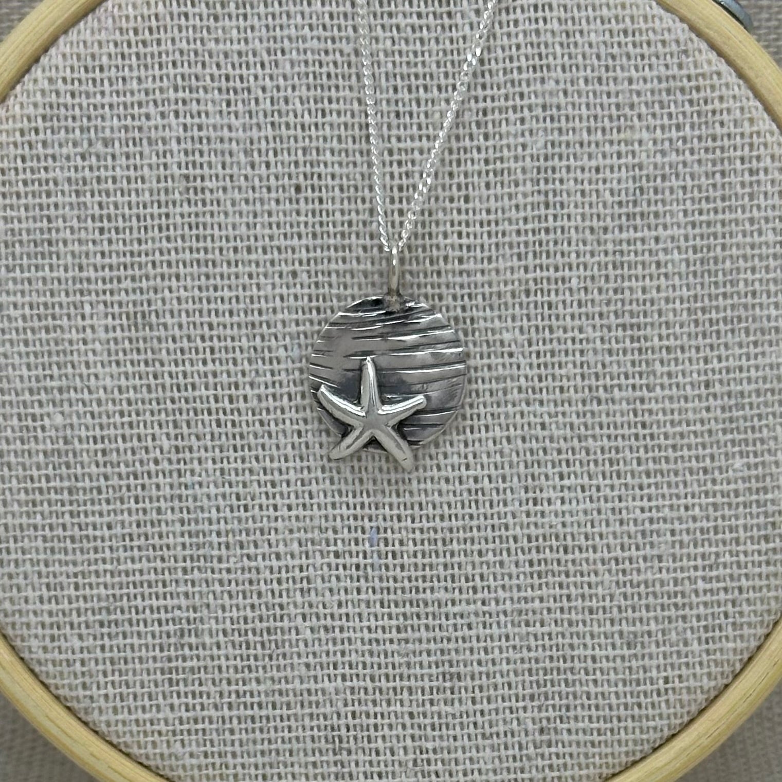 Handmade sterling silver starfish pendant with a textured coin background, displayed on an 18-inch silver curb chain
