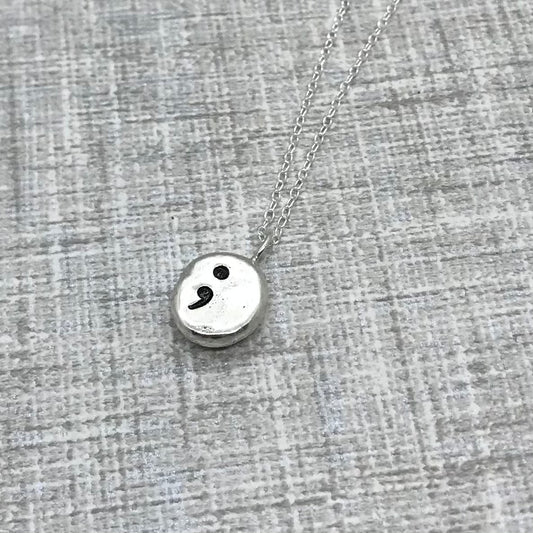 Handmade sterling silver pebble necklace featuring a hand-stamped semi-colon on one side, displayed on an 18-inch silver trace chain