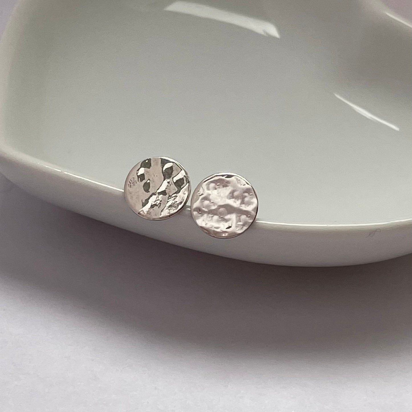 Close-up of small hammered silver disc stud earrings, showing their unique light-catching texture