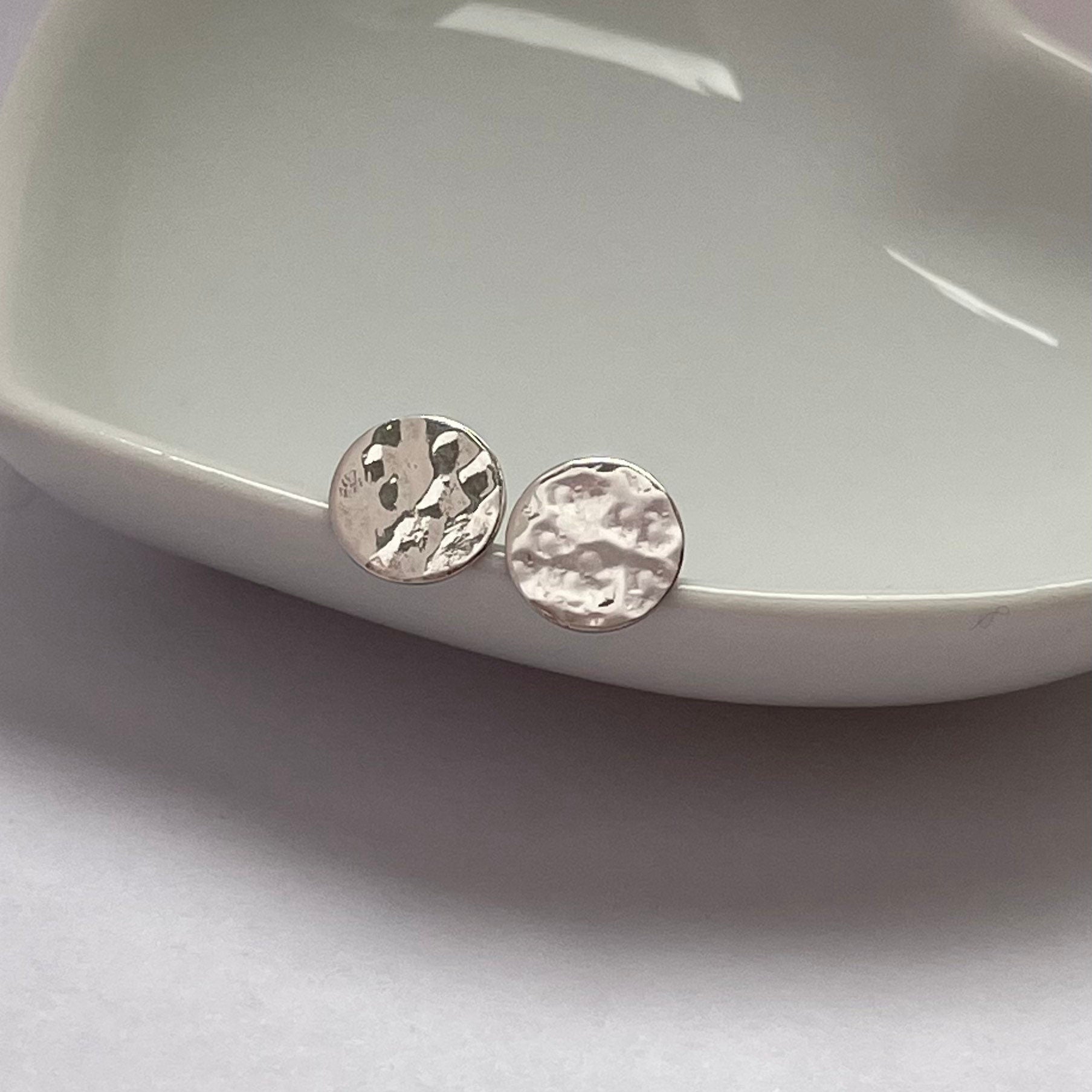 Close-up of small hammered silver disc stud earrings, showing their unique light-catching texture