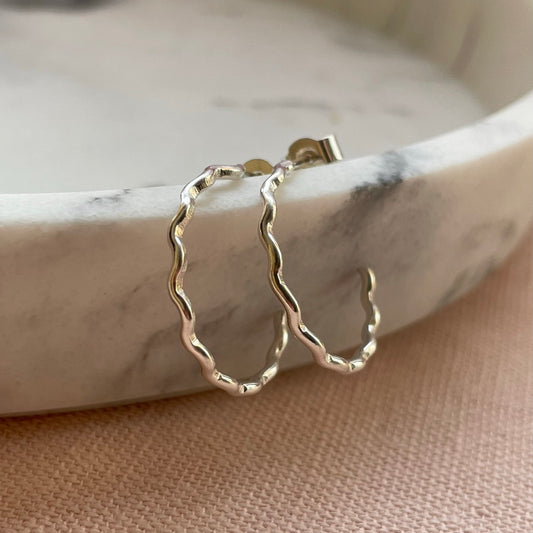 Handmade sterling silver open hoop earrings with a wavy, minimalist design, displayed against a white background